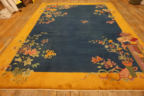 Floral rug with a blue field and yellow border lays on wide plank wooden floorboards.