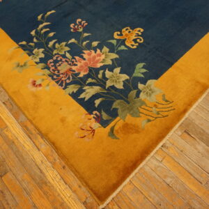 Navy blue rug with a gold border and pink floral design rests on rustic, worn hardwood floors.