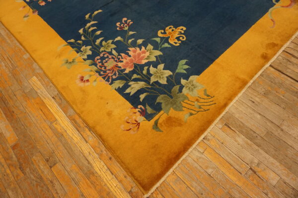Navy blue rug with a gold border and pink floral design rests on rustic, worn hardwood floors.