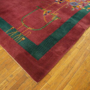 Magenta rug with a teal border and multi-colored floral and bird pattern on light brown hardwood flooring.