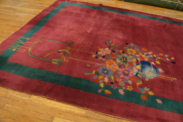 Magenta rug with a teal border and multi-colored floral and bird pattern on light brown wood floor