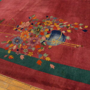 Magenta rug with a teal border and multi-colored floral and bird pattern on light brown hardwood flooring.
