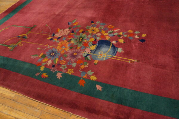 Magenta rug with a teal border and multi-colored floral and bird pattern on light brown hardwood flooring.