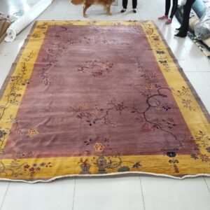 Dusty rose rug with gold border and floral pattern lies on a white tiled floor.