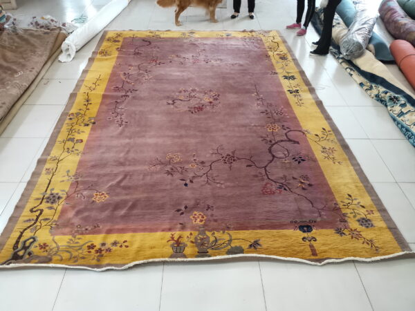 Dusty rose rug with gold border and floral pattern lies on a white tiled floor.