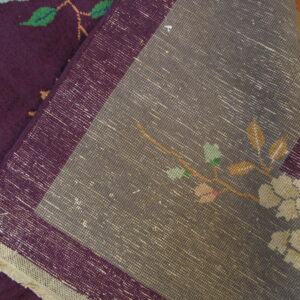 Deep purple rug pile with floral motifs is folded over the gray woven backing on wood planks.