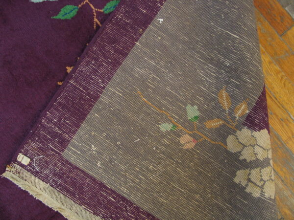 Deep purple rug pile with floral motifs is folded over the gray woven backing on wood planks.