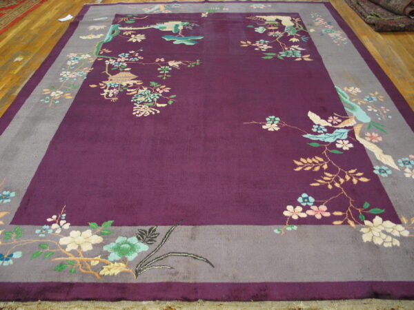 Plum-colored rug with gray borders featuring scattered flowering branches and birds on a wood floor.