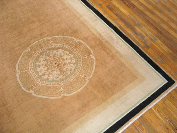 Tan rug corner with a cream medallion and border stripes in black, beige, and light green on wood planks.