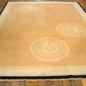 Large tan rug with three pale medallions and a striped border, lying flat on wide plank hardwood flooring.