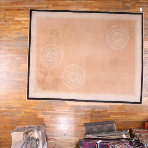 Low-pile peach rug with three large white medallions and a black border on distressed hardwood flooring.