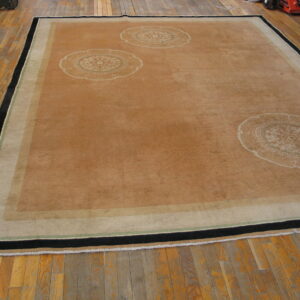 Large brown rug with circular motifs and a black, green, and tan border resting on distressed hardwood flooring.