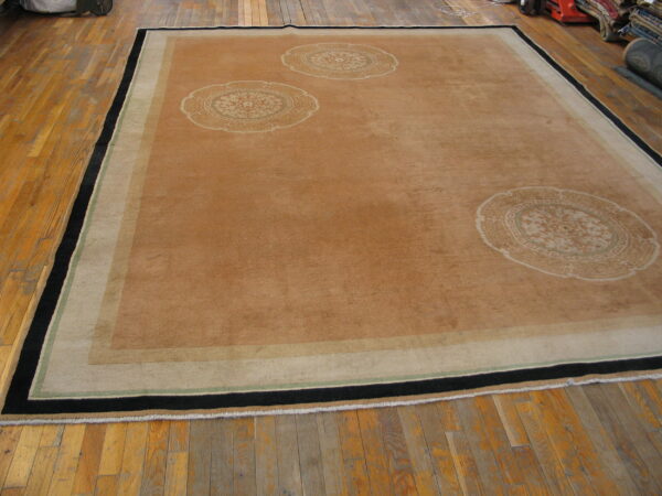 Large brown rug with circular motifs and a black, green, and tan border resting on distressed hardwood flooring.