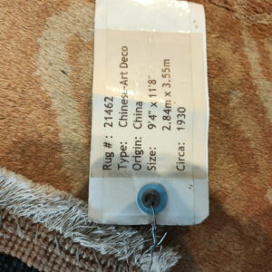 Detailed view of a sales tag secured to a high-pile rug showing brown and tan colors and white fringe.