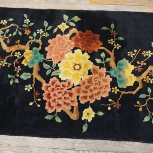 Black rug with a plush pile and a large multicolor floral branch design on wooden floorboards.