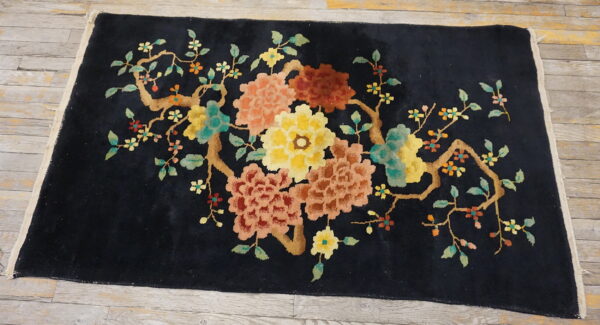 Black rug with a plush pile and a large multicolor floral branch design on wooden floorboards.