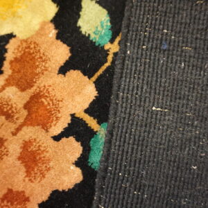 Close-up of a rug edge with orange, yellow, and green floral patterns against a dark ribbed woven side.