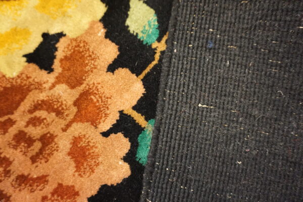 Close-up of a rug edge with orange, yellow, and green floral patterns against a dark ribbed woven side.
