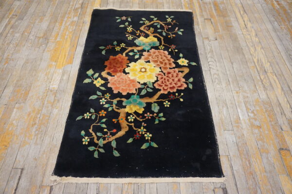 Black runner rug featuring yellow, coral, and teal floral branches laid on distressed wooden flooring.