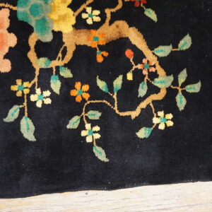 Black high-pile rug with peach, yellow, and green floral motifs rests on light wood planks.