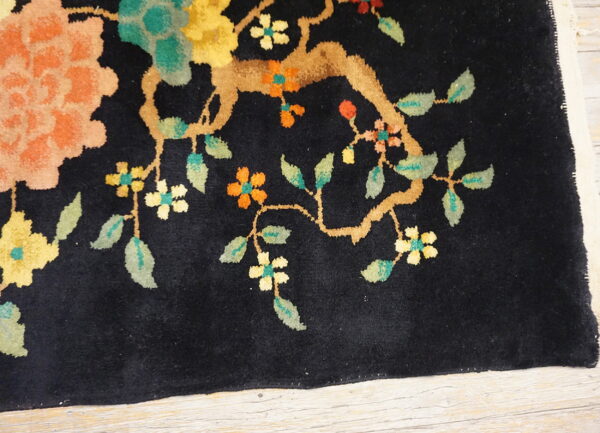 Black high-pile rug with peach, yellow, and green floral motifs rests on light wood planks.