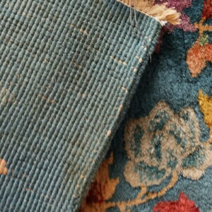 High-pile teal rug with multicolored floral design folded over its ribbed blue-green backing.