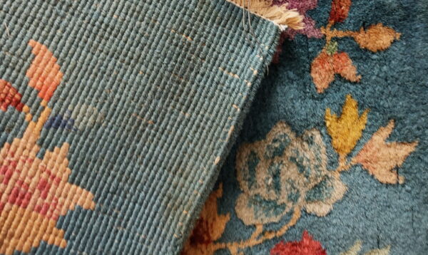 High-pile teal rug with multicolored floral design folded over its ribbed blue-green backing.