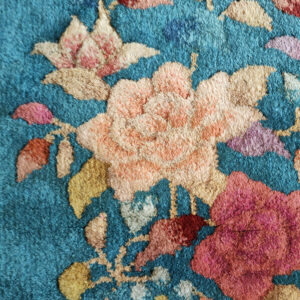 Textured teal rug with multicolor floral patterns, showing the ribbed woven backing, fringe, and attached tag.