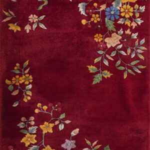 A deep red plush rug featuring corner clusters of colorful yellow, green, and blue florals.