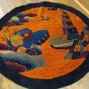 Round rug with a navy blue border and an orange field displaying a colorful scenic design on wood floors.