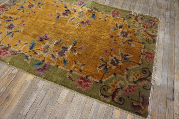 Gold low-pile rug with a decorative green border featuring multi-colored floral designs on distressed wood.