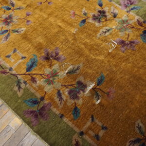 Mustard yellow rug featuring an elaborate floral design and a moss green border rests on weathered wooden planks.