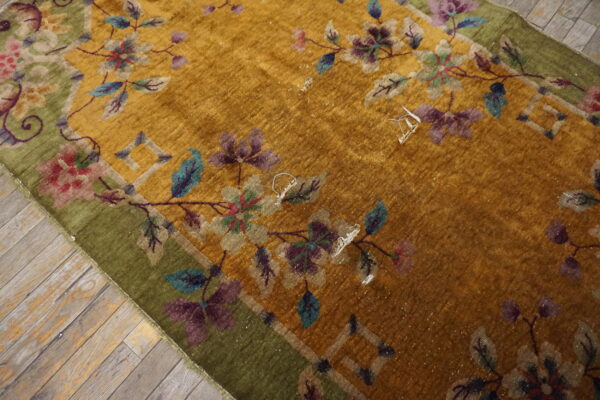 Mustard yellow rug featuring an elaborate floral design and a moss green border rests on weathered wooden planks.