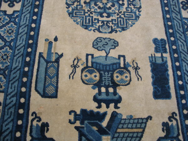 Close-up of a low-pile rug featuring stylized vessels and symbols in shades of blue on a cream background, surrounded by a complex blue border.