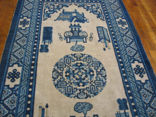 An off-white rug with complex blue geometric and pictorial motifs rests on a glossy hardwood floor.