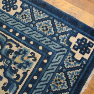 Navy and light blue patterned rug corner with cream accents rests on natural wood flooring.