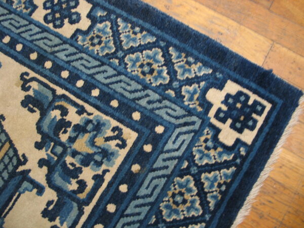 Navy and light blue patterned rug corner with cream accents rests on natural wood flooring.