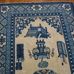 Blue and cream rug with geometric borders and stylized patterns on a glossy wood plank floor.