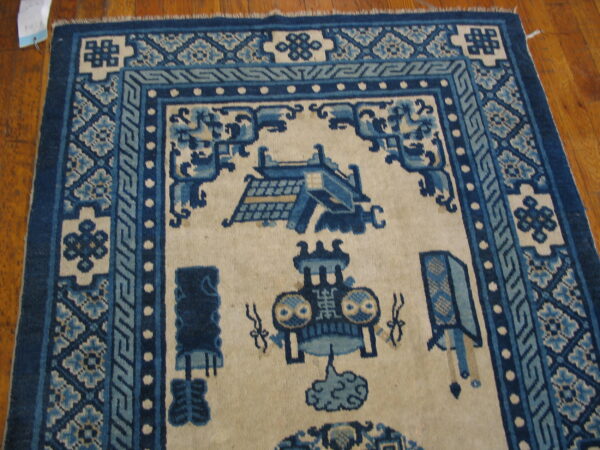 Blue and cream rug with geometric borders and stylized patterns on a glossy wood plank floor.