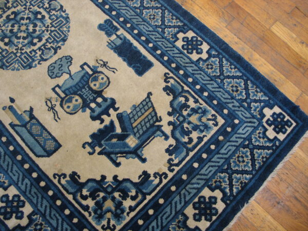 Blue and beige rug with stylized objects, medallions, and a detailed geometric border on wood planks.