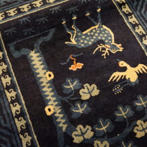 Dark blue high-pile rug with a detailed geometric border and central animal motifs in pale yellow and light blue.