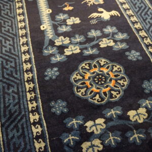 High-pile navy rug with blue, cream, and orange floral, bird, and geometric patterns on wood floors.