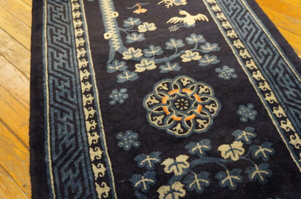 High-pile navy rug with blue, cream, and orange floral, bird, and geometric patterns on wood floors.