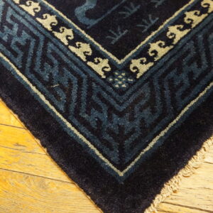 Navy blue rug corner with teal and cream geometric borders rests on yellow wood flooring.