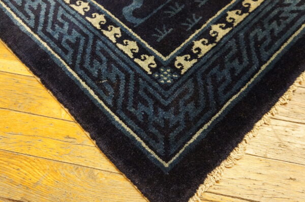 Navy blue rug corner with teal and cream geometric borders rests on yellow wood flooring.
