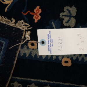 Dark navy hand-woven wool rug detail featuring olive and coral floral patterns and product tag.