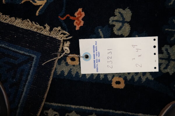 Dark navy hand-woven wool rug detail featuring olive and coral floral patterns and product tag.