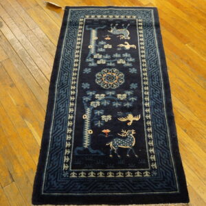 Dark blue runner rug featuring detailed deer, birds, and floral patterns sits on distressed hardwood flooring.