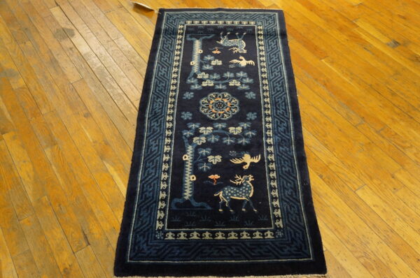 Dark blue runner rug featuring detailed deer, birds, and floral patterns sits on distressed hardwood flooring.