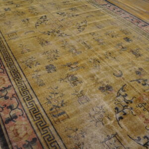 Faded gold rug featuring scattered dark traditional designs and a pink patterned border on wood floor.